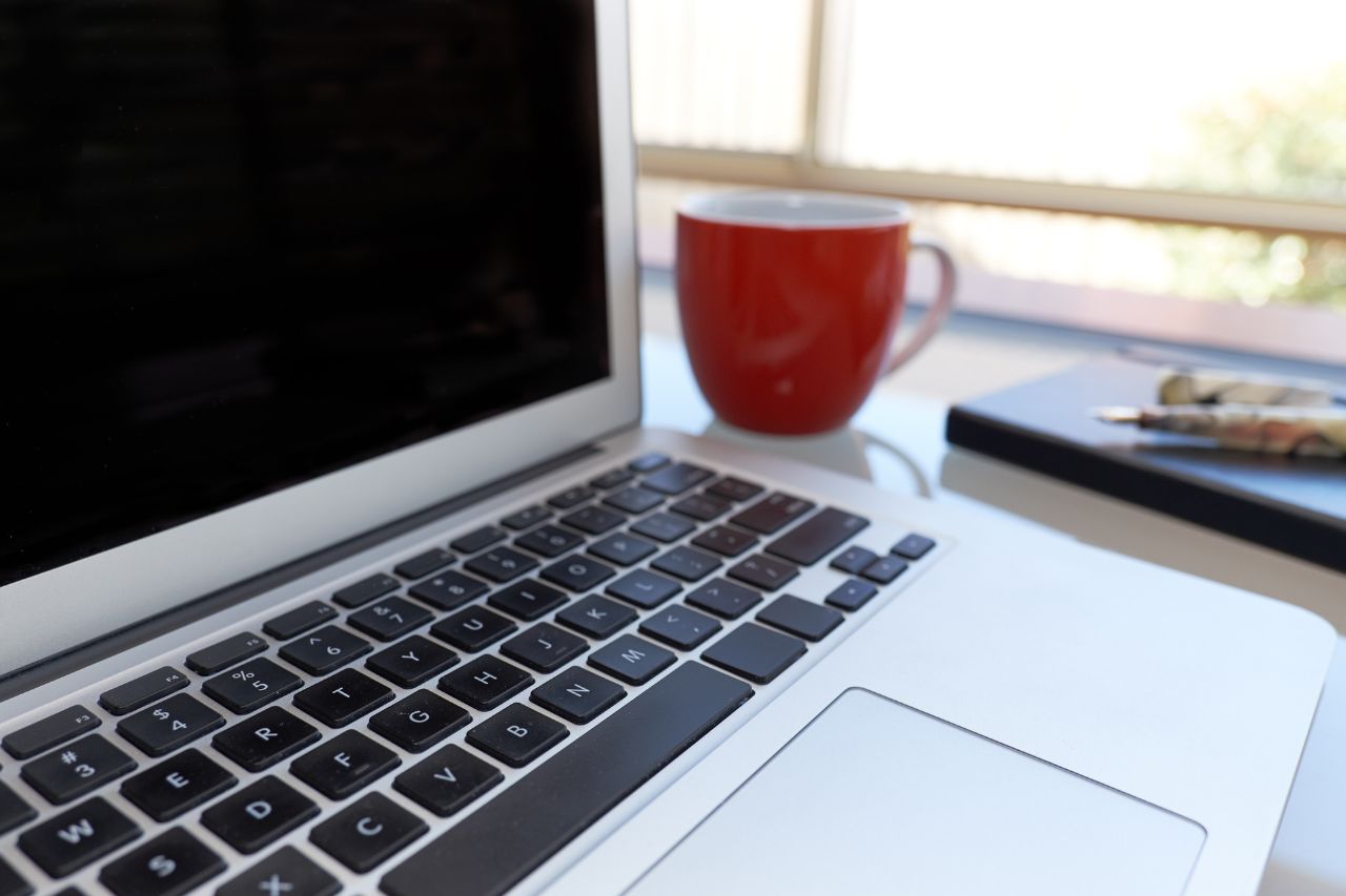 image of a laptop on a desk with a red mug next to it.