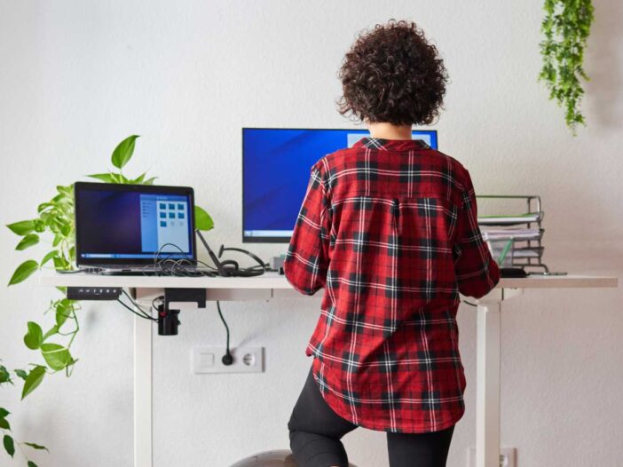 Sit stand desks - Unrecognizable woman teleworking at an adjustable standing desk with one knee resting on a fitball