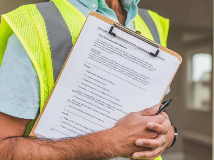 Man in high visibility jacket holding inspection checklist on clipboard.