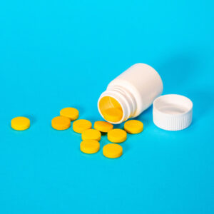 Spilled pot of yellow pills on a blue background