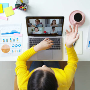 a woman on a laptop having a video conference with a hot drink, graphs, post-its, pens and notebooks beside her