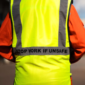 The back of a person in a high visibility jacket with 'stop work if unsafe' on the back.