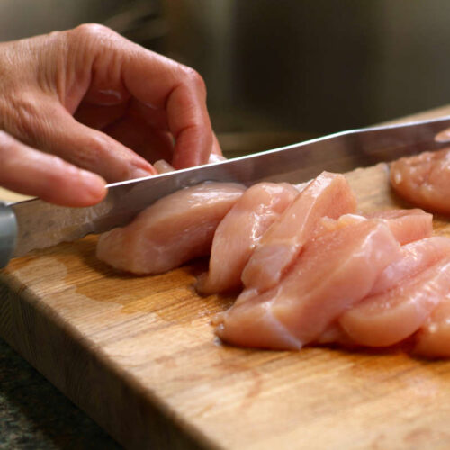 Person cutting raw chicken on a chopping board to illustrate food safety practices.