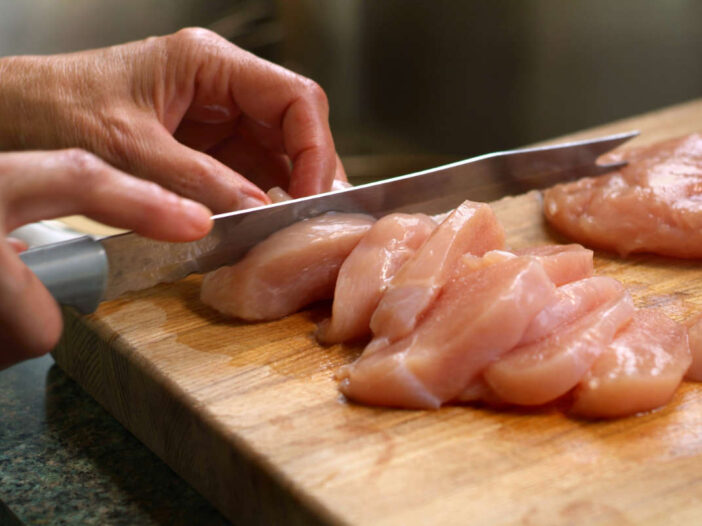 Person cutting raw chicken on a chopping board to illustrate food safety practices.