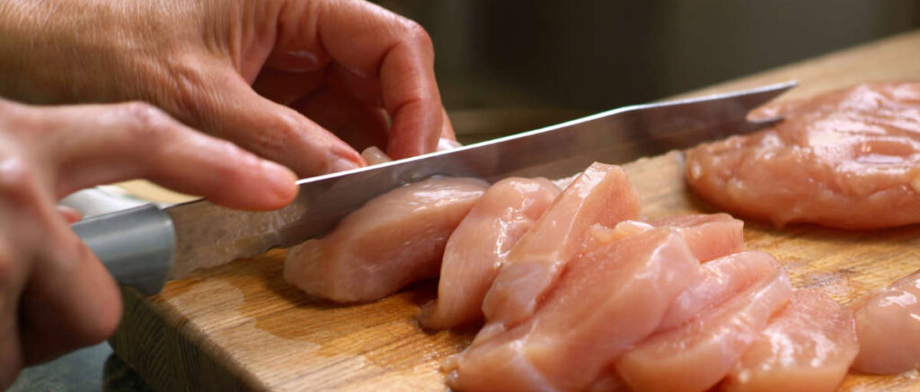 Person cutting raw chicken on a chopping board to illustrate food safety practices.