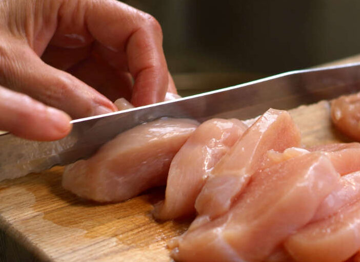 Person cutting raw chicken on a chopping board to illustrate food safety practices.