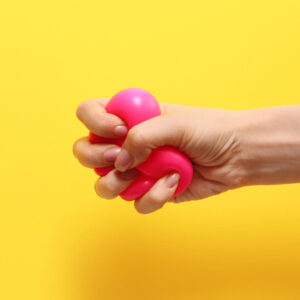 Hand on a yellow background tightly squeezing a red stress ball to illustrate stress awareness training for managers.