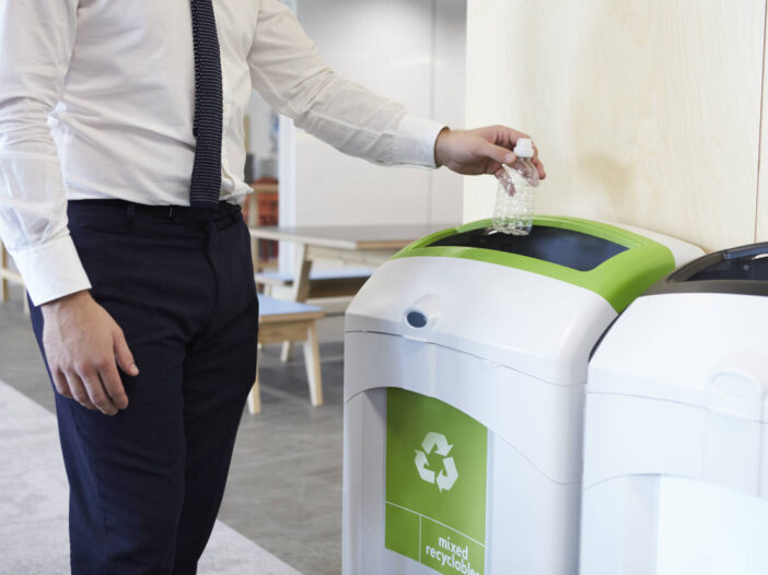 environmental awareness at work – Man in an office throwing plastic bottle into recycling bin