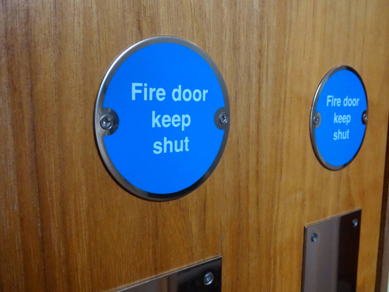 Fire door regulations – Photo showing a circular blue sign with white writing saying 'Fire Door Keep Shut '.