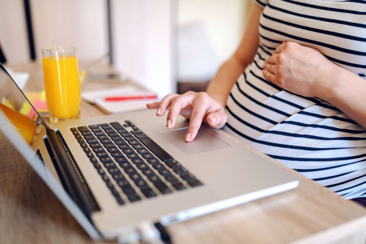 Pregnancy risk assessment Close up of pregnant worker using laptop