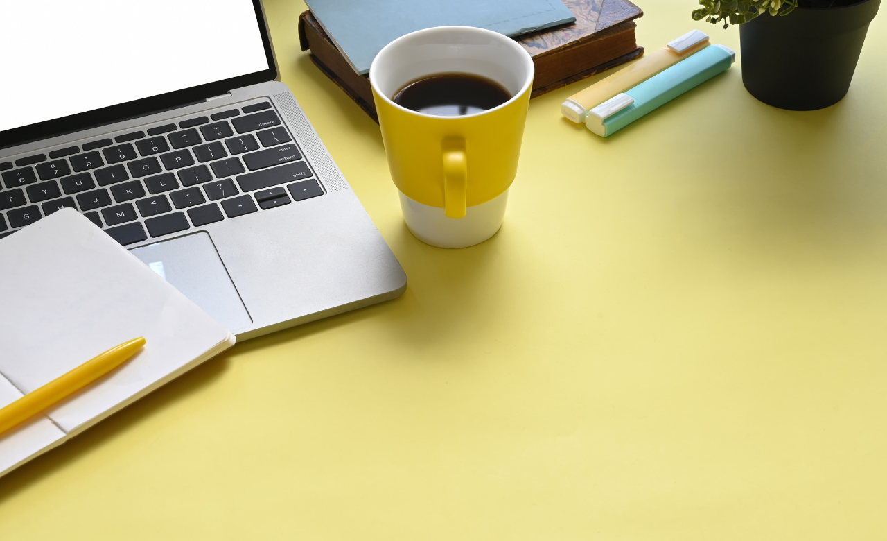 image of a laptop on a desk with a mug of coffee and a notebook adjacent to it.