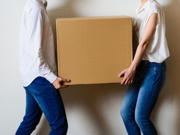 Two people working together to carry a box to show safe team lifting.