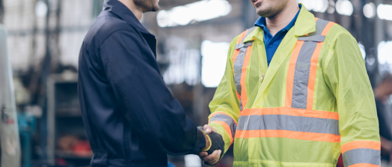 Two workmen in a warehouse shaking hands.