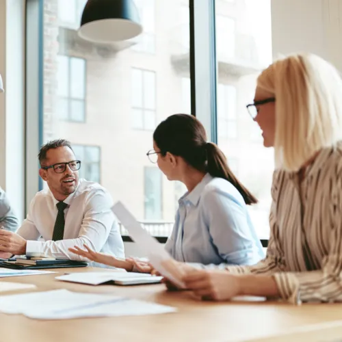 Three smiling directors and executives in a boardroom having a discussion while holding paper.