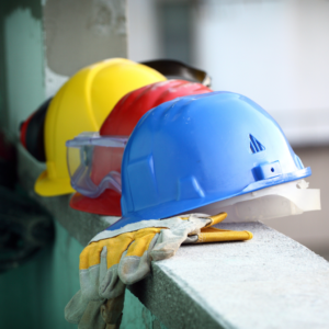 Three hard hats on a ledge - red, yellow and blue with protective gloves.