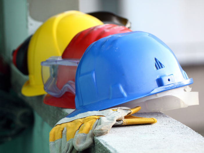Three hard hats on a ledge - red, yellow and blue with protective gloves.