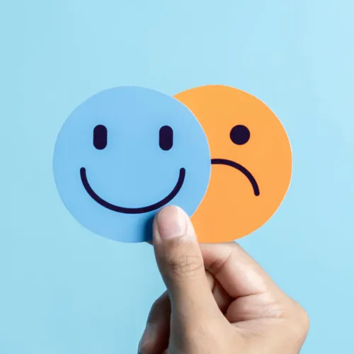 Hand holding a blue circular smiling face and an orange sad face to symbolise managing occupational health and wellbeing.