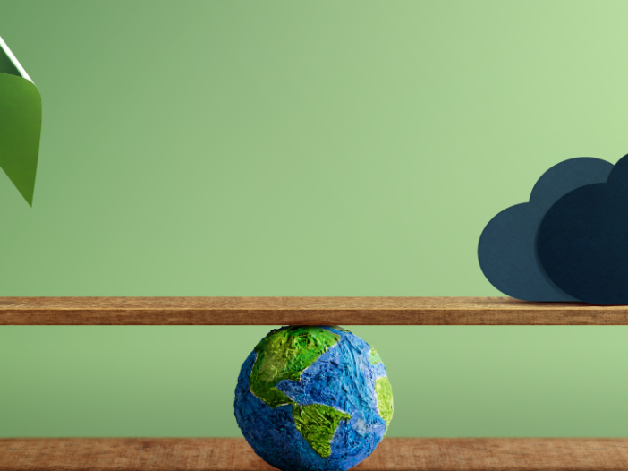 Environmental symbol of the globe beneath a seesaw balancing a paper windmill and a CO2 cloud