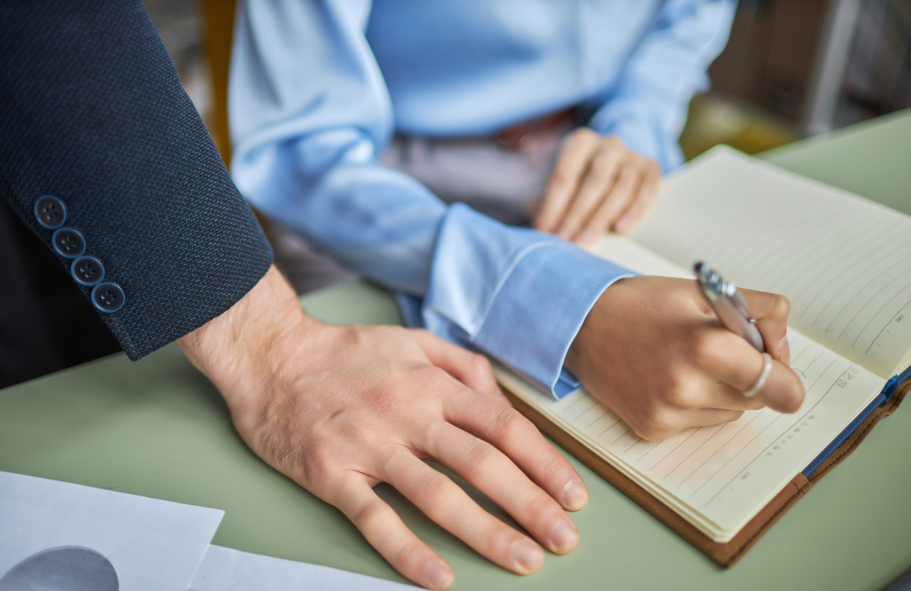 What is sexual harassment in the workplace? Illustrating a man's hand very close to a woman's hand as she works.