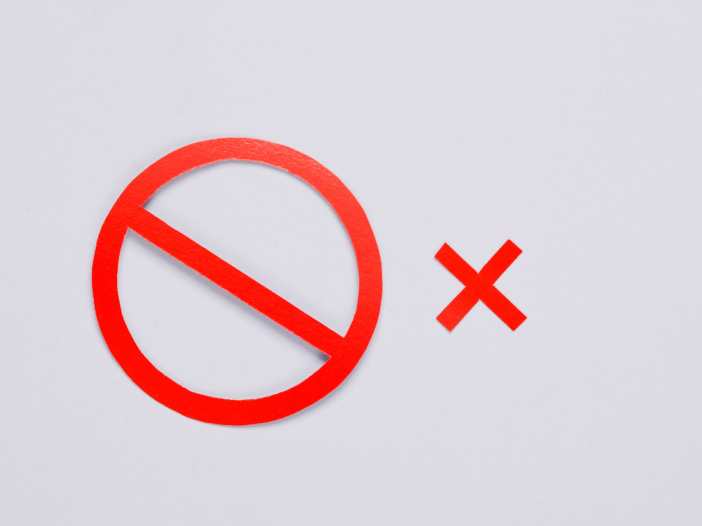 Two red paper symbols next to each other - one is a cross and the other is a no entry sign to symbolise a prohibition notice.