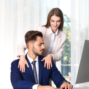 Man and woman in workplace. Woman with hands on man's shoulders while he looks uncomfortable. Symbolising sexual harassment in the workplace.