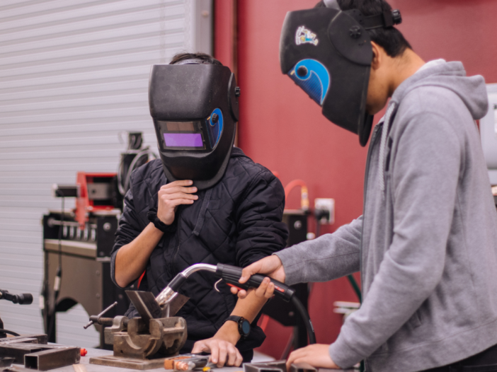 Two people in PPE - one demonstrating how to use a machine to illustrate PUWER training requirements.