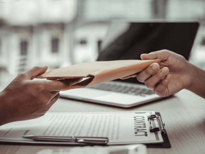 One person handing an envelope to another to demonstrate fraud.