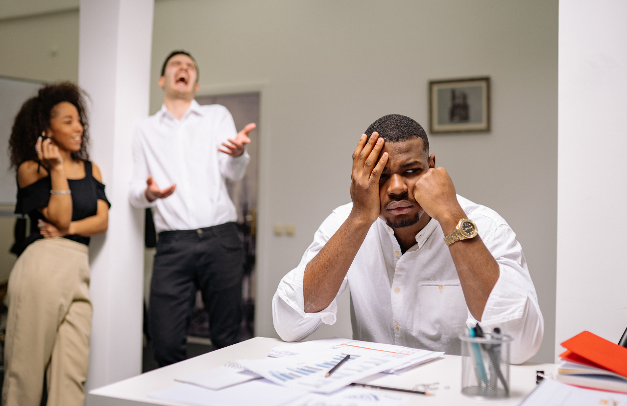 Image showing a man and woman laughing while another man is at his desk looking uncomfortable