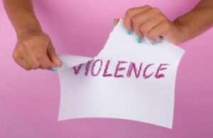 Woman ripping up a piece of paper with the word 'violence' written on it against a pink background