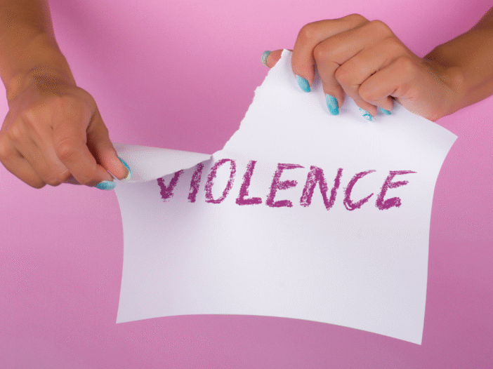 Woman ripping up a piece of paper with the word 'violence' written on it against a pink background