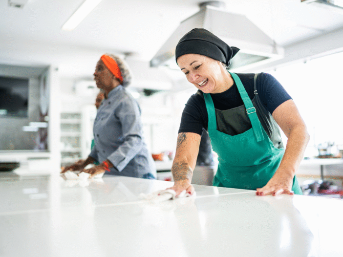 Two women in a commercial kitchen cleaning a surface to illustrate 'clean as you go'