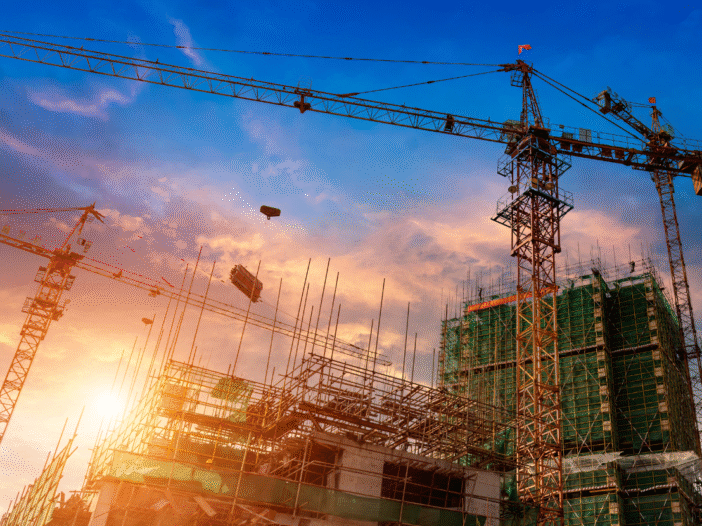 Construction site at dawn showing cranes against skyline