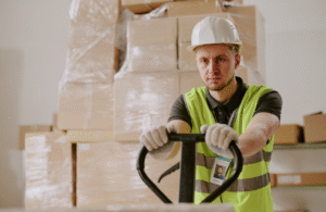 Man in PPE in warehouse using machinery to lift boxes