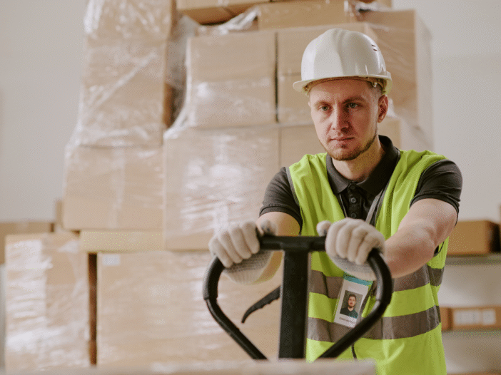 Man in PPE in warehouse using machinery to lift boxes