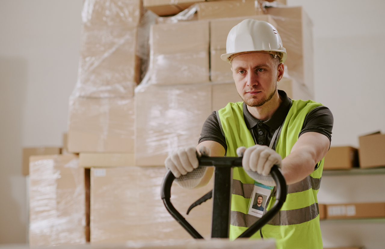 Man in PPE in warehouse using machinery to lift boxes