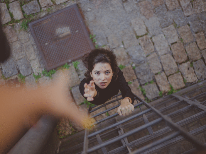Woman reaching up to an outstretched hand as she is about to climb a ladder