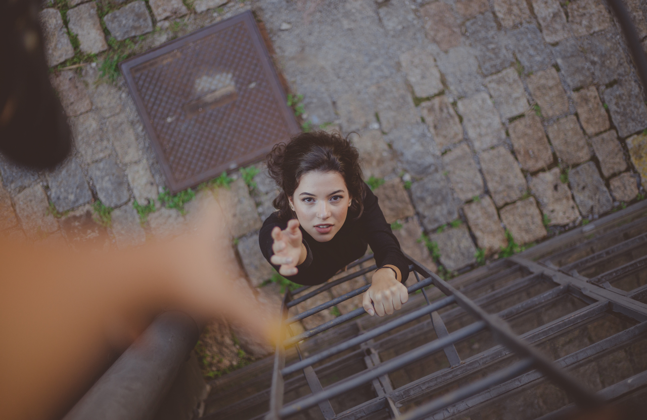 Woman reaching up to an outstretched hand as she is about to climb a ladder
