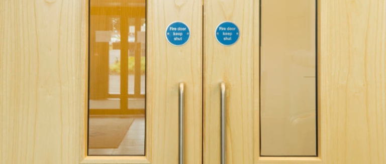Fire Door Inspection course image - a close-up of a set of UK Fire Doors, with blue circular signs and clouded windows.