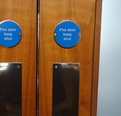Fire Door Inspection course thumb - a close-up of a set of UK Fire Doors, with blue circular signs and clouded windows.
