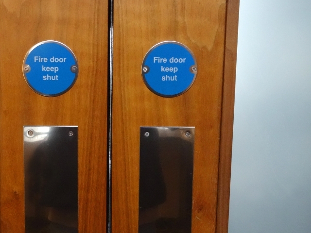 Fire Door Inspection course thumb - a close-up of a set of UK Fire Doors, with blue circular signs and clouded windows.