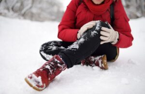 Preventing slips, trips and falls in winter workplace guide - main image. A person wearing winter clothes has fallen in snow, and is clutching their knee in pain.