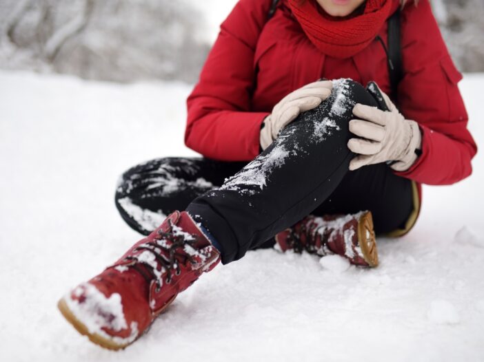 Preventing slips, trips and falls in winter workplace guide - main image. A person wearing winter clothes has fallen in snow, and is clutching their knee in pain.