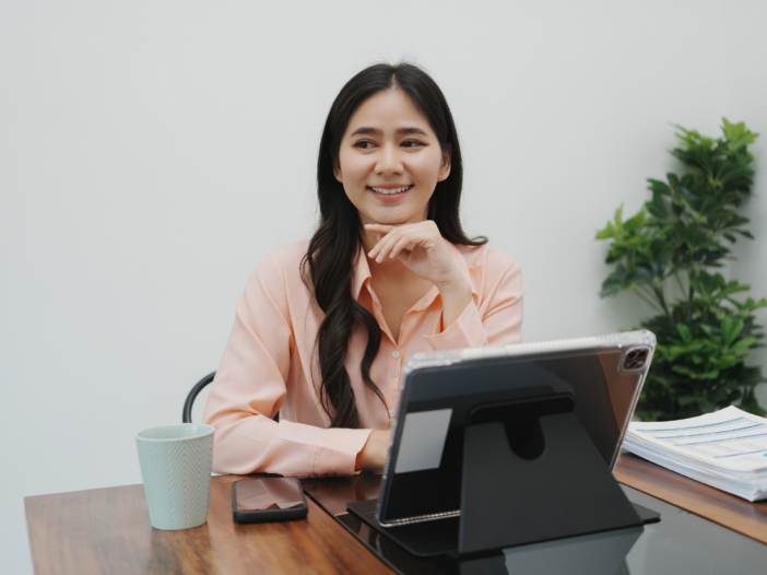 Woman at her desk with laptop smiling at camera, happy at work for World Wellbeing Week
