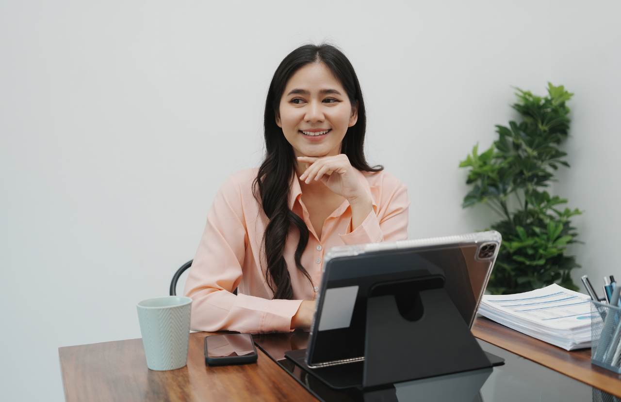 Woman at her desk with laptop smiling at camera, happy at work for World Wellbeing Week