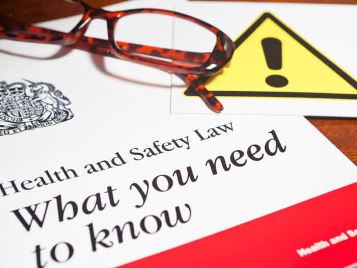 Booklet entitled, 'Health and Safety Law: What you need to know' with glasses and a caution sign overlapping. Symbolises list of health and safety legislation uk
