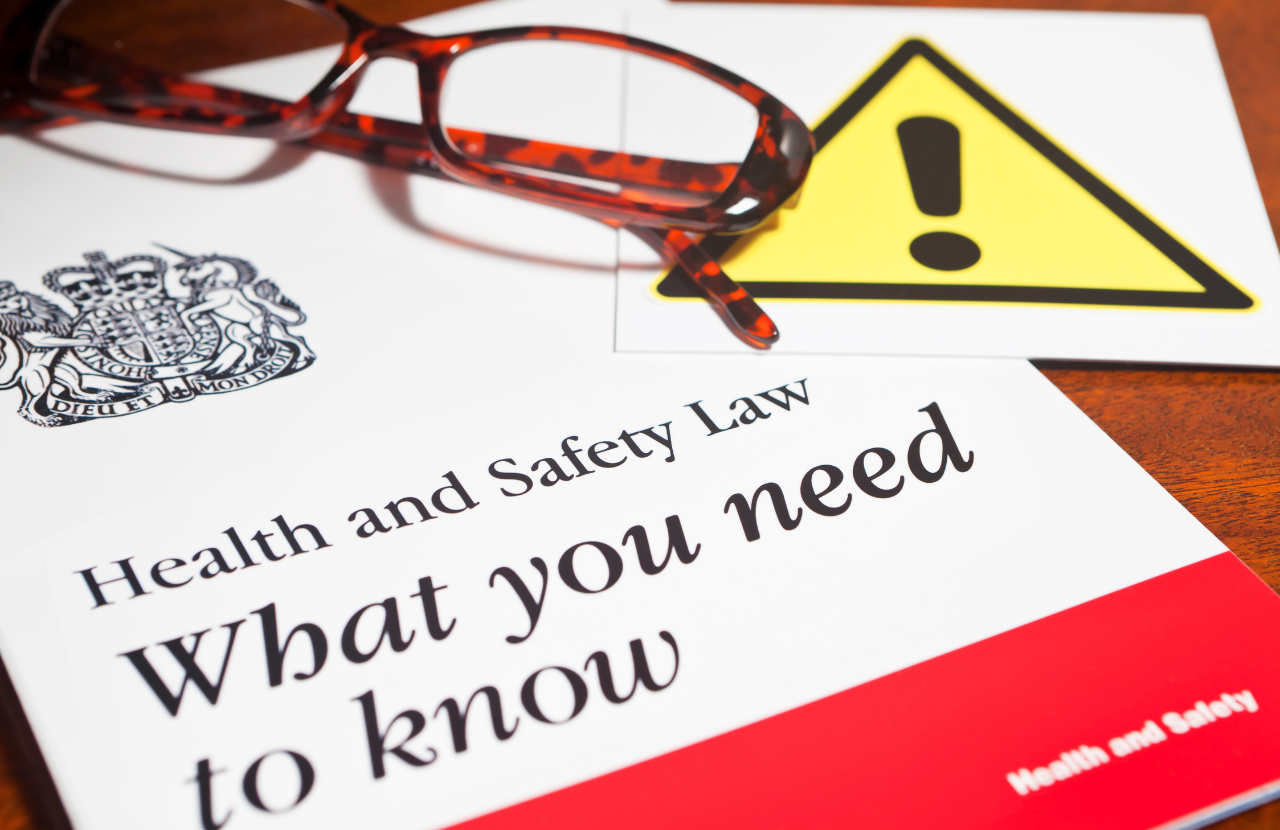 Booklet entitled, 'Health and Safety Law: What you need to know' with glasses and a caution sign overlapping. Symbolises list of health and safety legislation uk