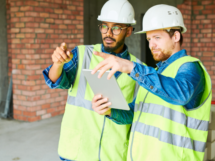 Two construction workers discussing something on an ipad and pointing into the distance, to illustrate pre construction notification
