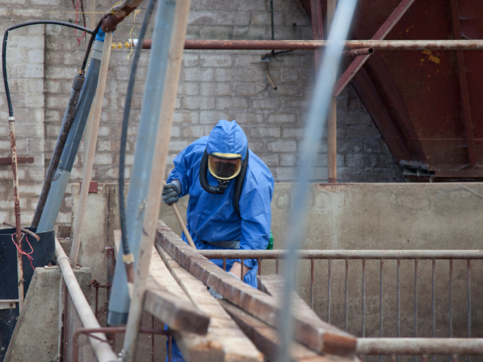 Man in full PPE removing asbestos from roof space to illustrate asbestos register.