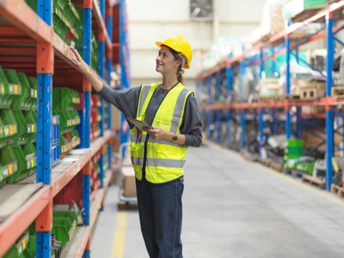 Female worker in a warehouse in PPE searching shelves to represent workers responsibility for health and safety at work