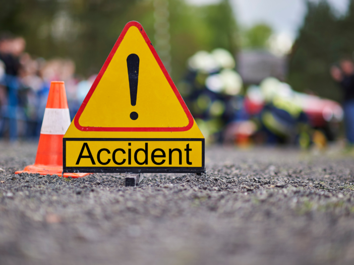 Accident sign and cone in the middle of a road or path. The accident and people behind are blurred out. Illustrates root cause analysis examples